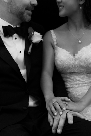 a black and white photograph that is cropped to feature the bride and groom's wedding rings. the bride and groom are looking at each other and smiling