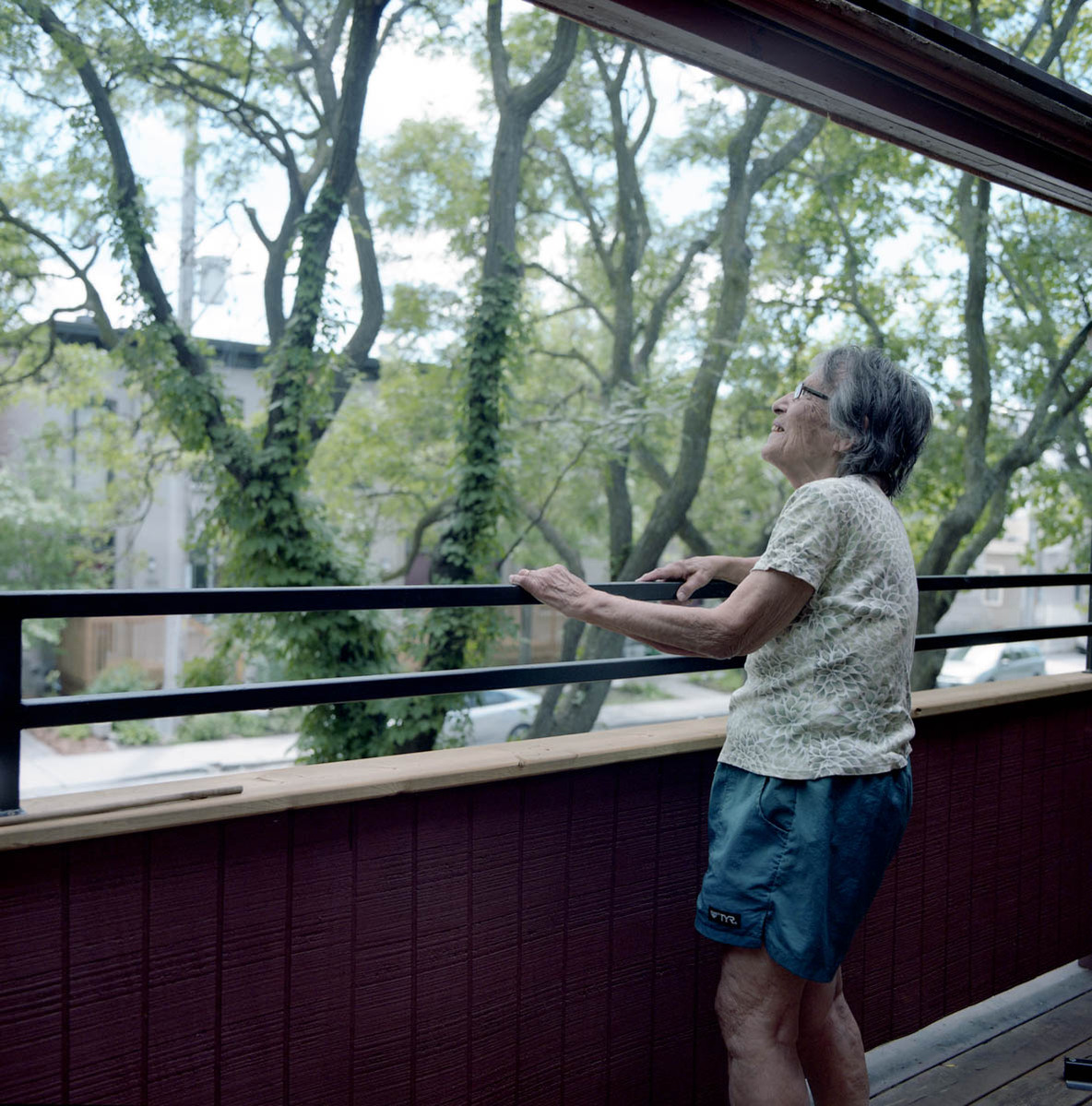 an elderly woman, clad in shorts and t-shirt, on the front deck of her home staring at the trees; part of a series on Medical Assistance in Dying