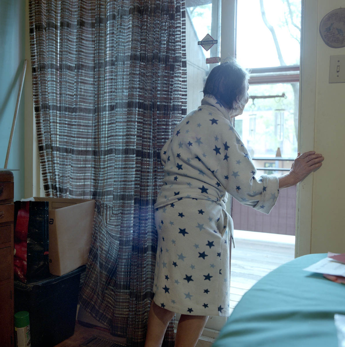 an elderly woman, clad in her bathrobe, looks out her window; part of a series on Medical Assistance in Dying