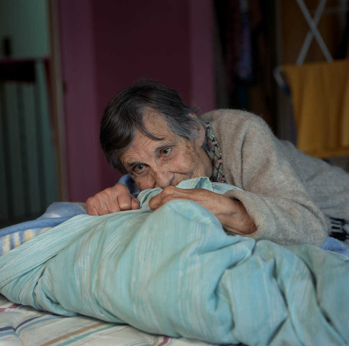 an elderly woman, looking anxious, is lying across her bed; part of a series on Medical Assistance in Dying