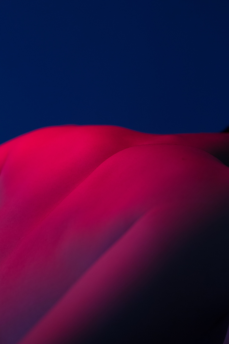 Back of the man in nude which looks like a mountain or ridges body is in the color magenta and background is in dark navy