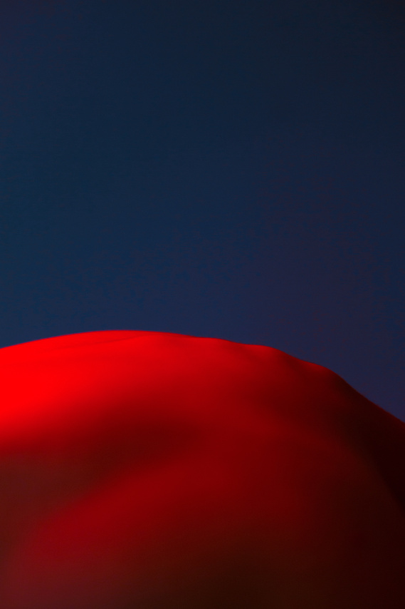 Man body in nude in red color and there is deep navy background it looks like a surreal landscape of a desert