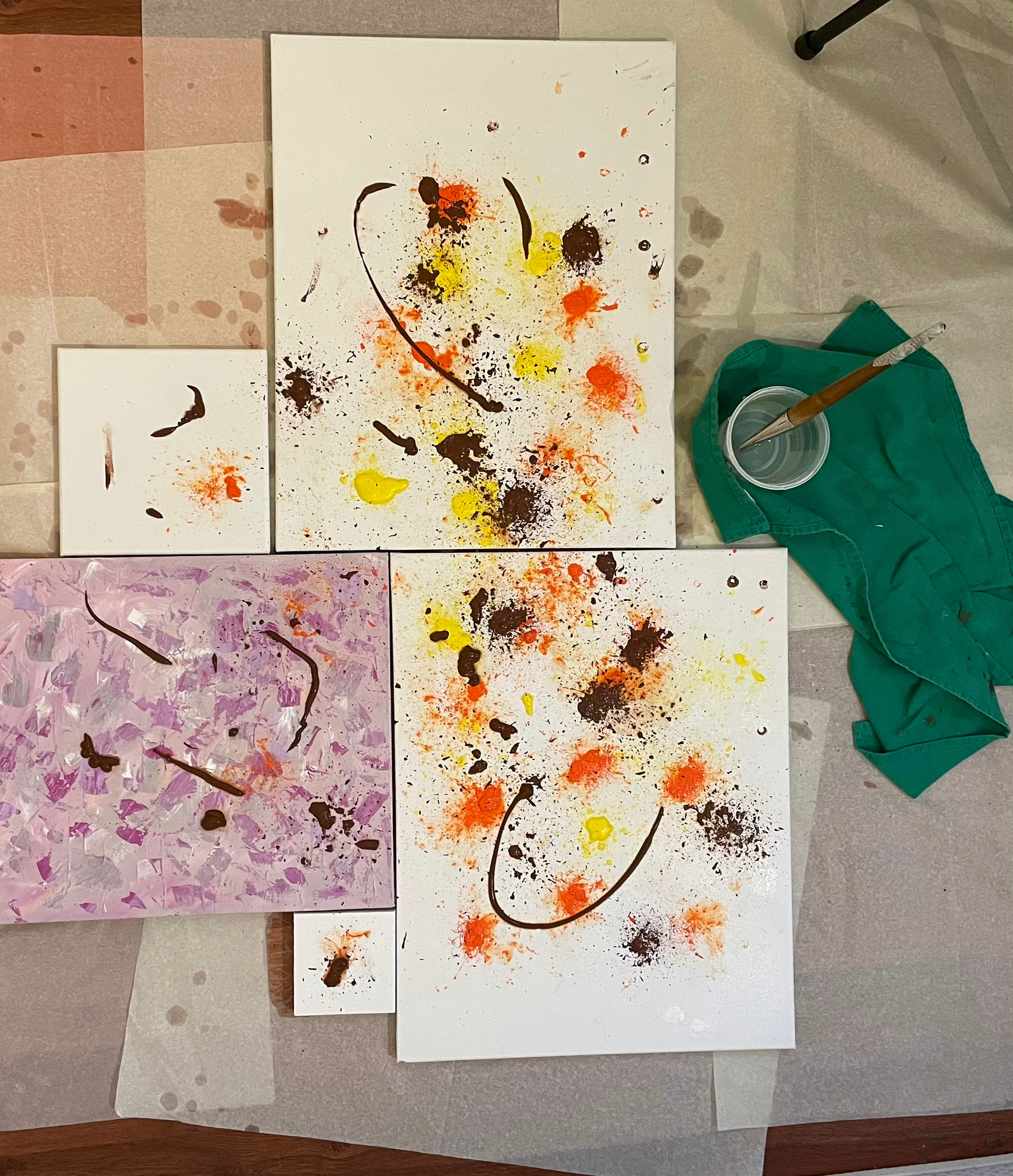 A collage of five stretched canvases on the floor along with a bowl of water, a painting brush and a rag on the right hand side.