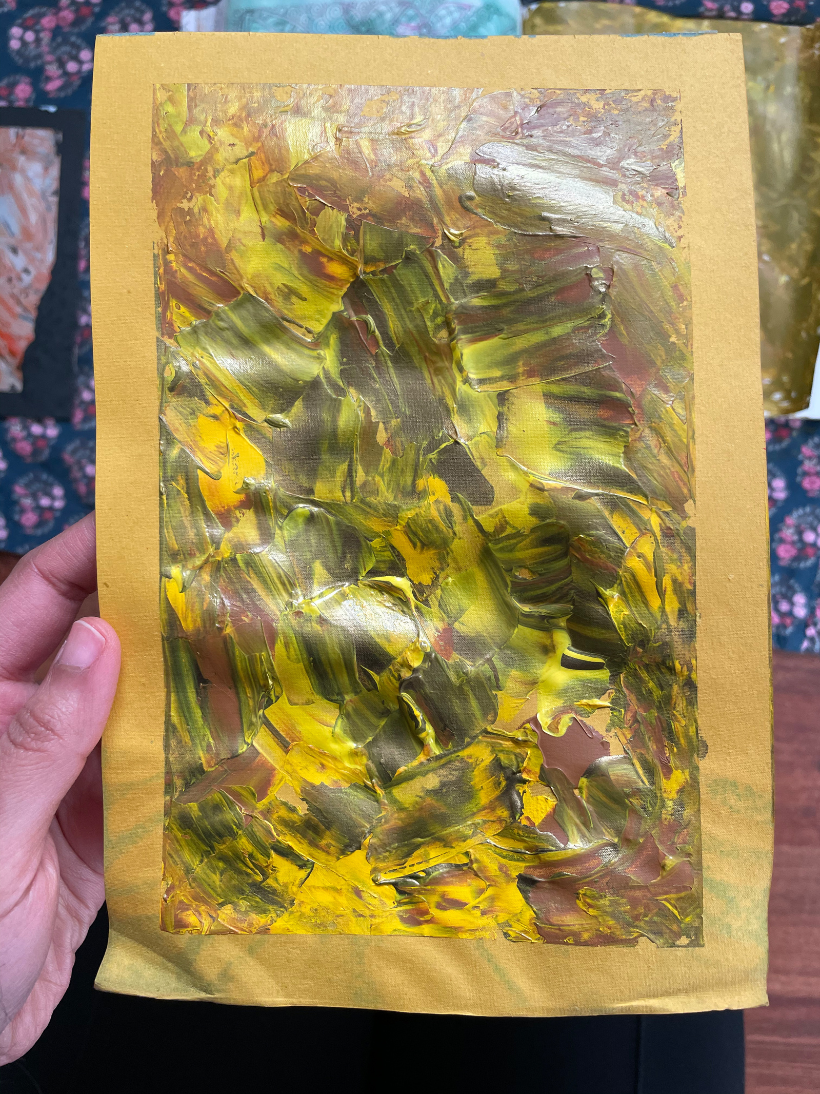 The artist's left hand holding a painting on a piece of paper for the camera. Artist is not in the frame. 