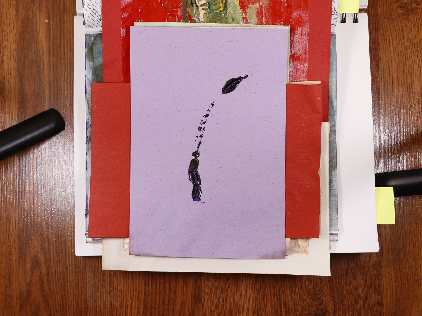A stack of paintings on the floor with studio lights on either sides.