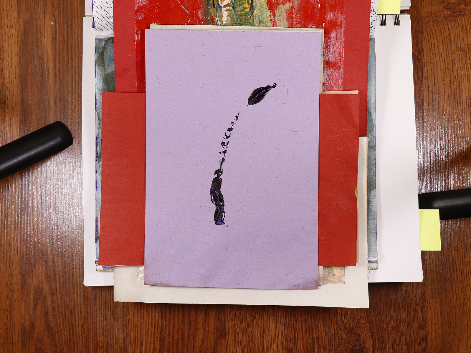 A stack of paintings on the floor with studio lights on either sides.