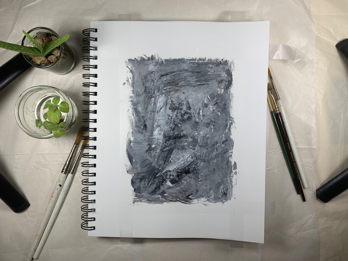 A studio setup with painting in the centre with small plants on the left side, brushes and studio lights on both the sides.