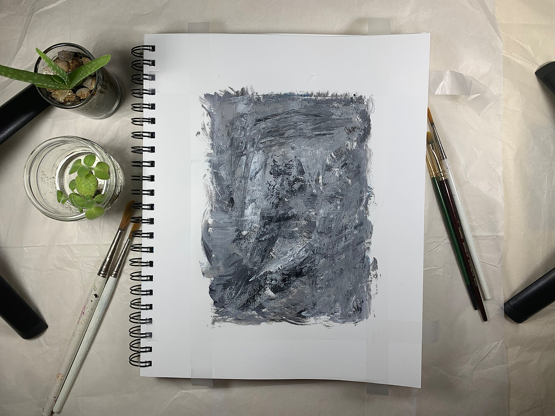 A studio setup with painting in the centre with small plants on the left side, brushes and studio lights on both the sides.