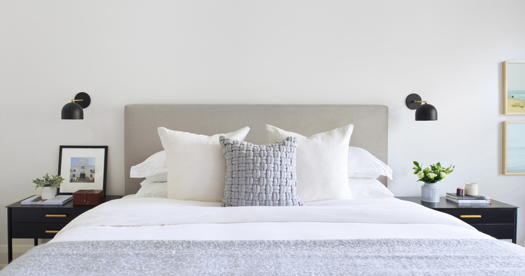 Bedroom design by ALC Interiors featuring upholstered grey headboard, white bedding, and modern black sconces.