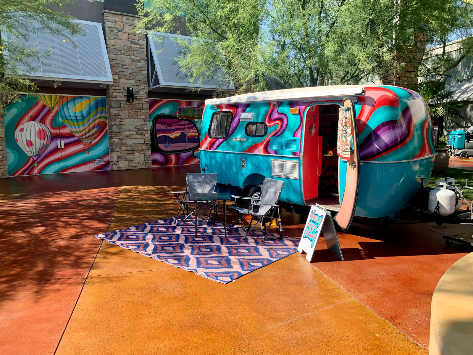 A painted travel-themed mural at Desert Ridge Marketplace by Kayla Newnam for Out There Murals 50 State Project with an art trailer.
