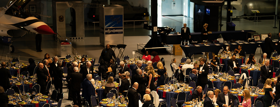 Black-tie corporate gala dinner with banquet tables in an aviation hangar venue