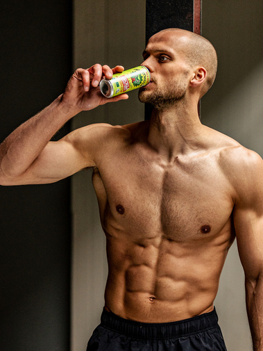fitness fotoshoot, een gespierde man die water drinkt tijdens een fotoshoot. Ontbloot bovenlichaam, kort haar. 
