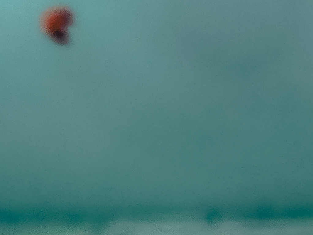 A red kite surf stands out against a blurred dark green / blue sea and stormy sky