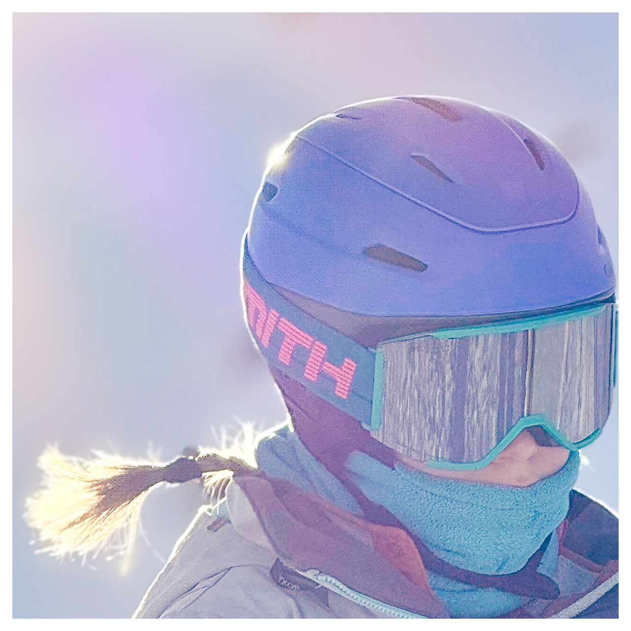 Head shot of a girl wearing ski gear stands against what appears a pastel sky