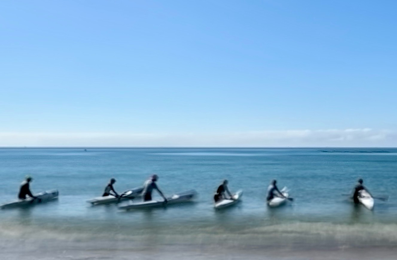 A group of surfers close to the shore line try and surf on what appears non-existent surf