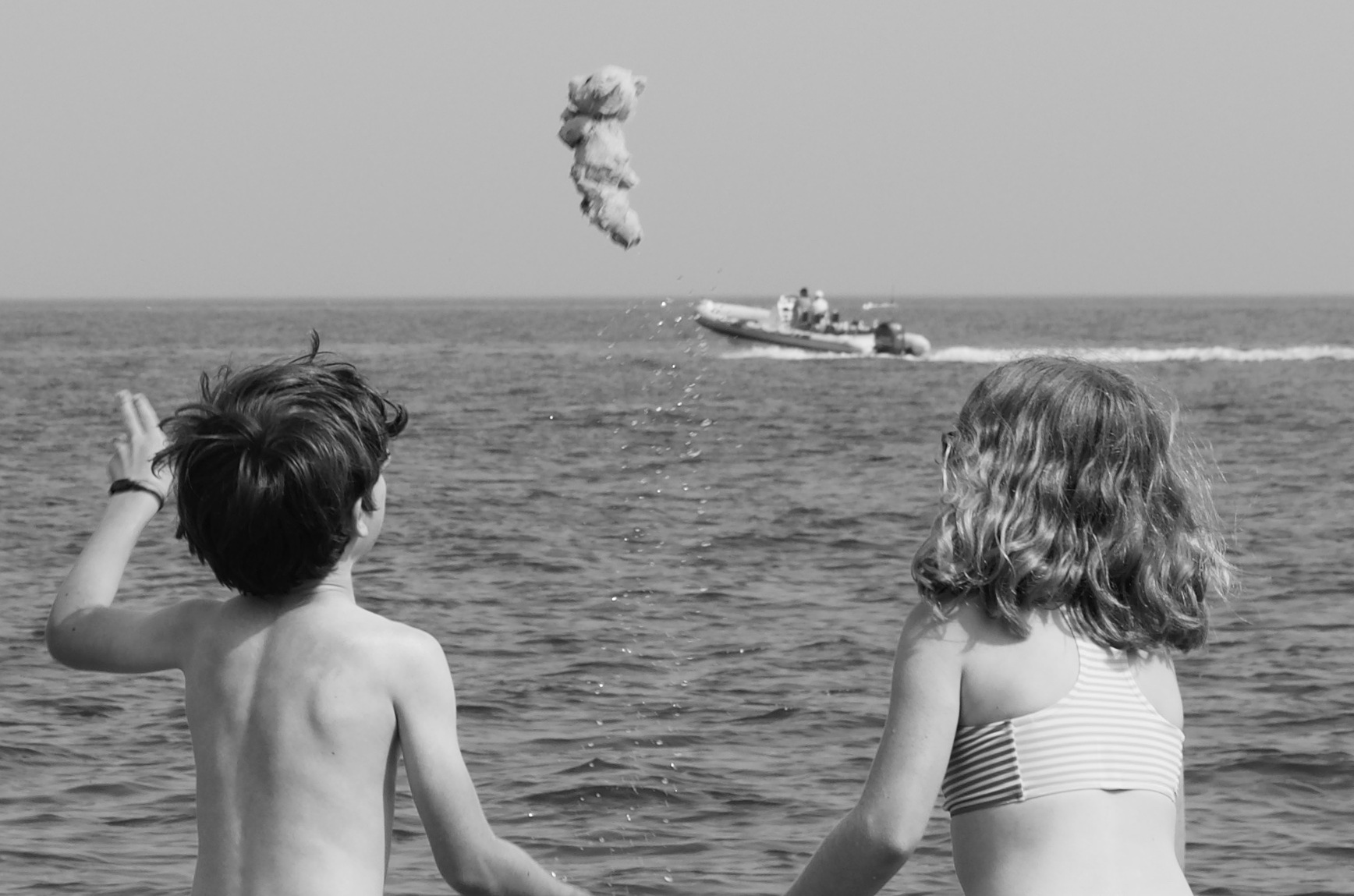 Kids playing on the beach a teddy bear is thrown and looks like it is about to land on a boat