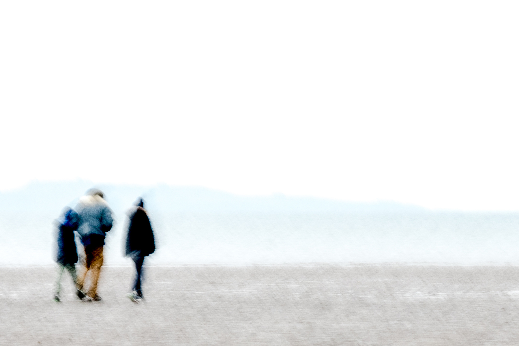 Three people walk across what looks like a wind swept beach in winter (Crammond, Edinburgh)