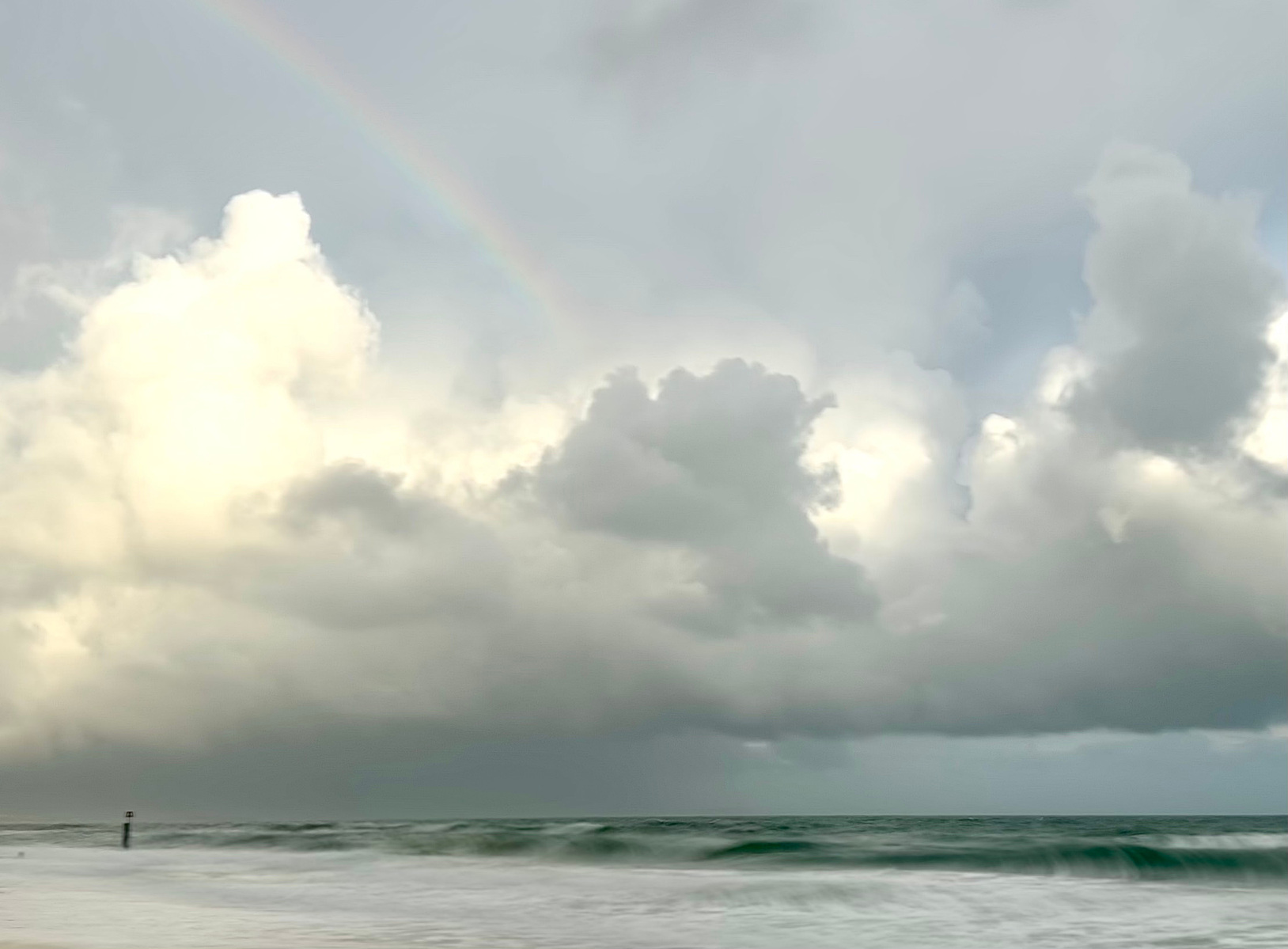Low cloud hang over a moody sea with a rainbow hitting the mid-third of the frame