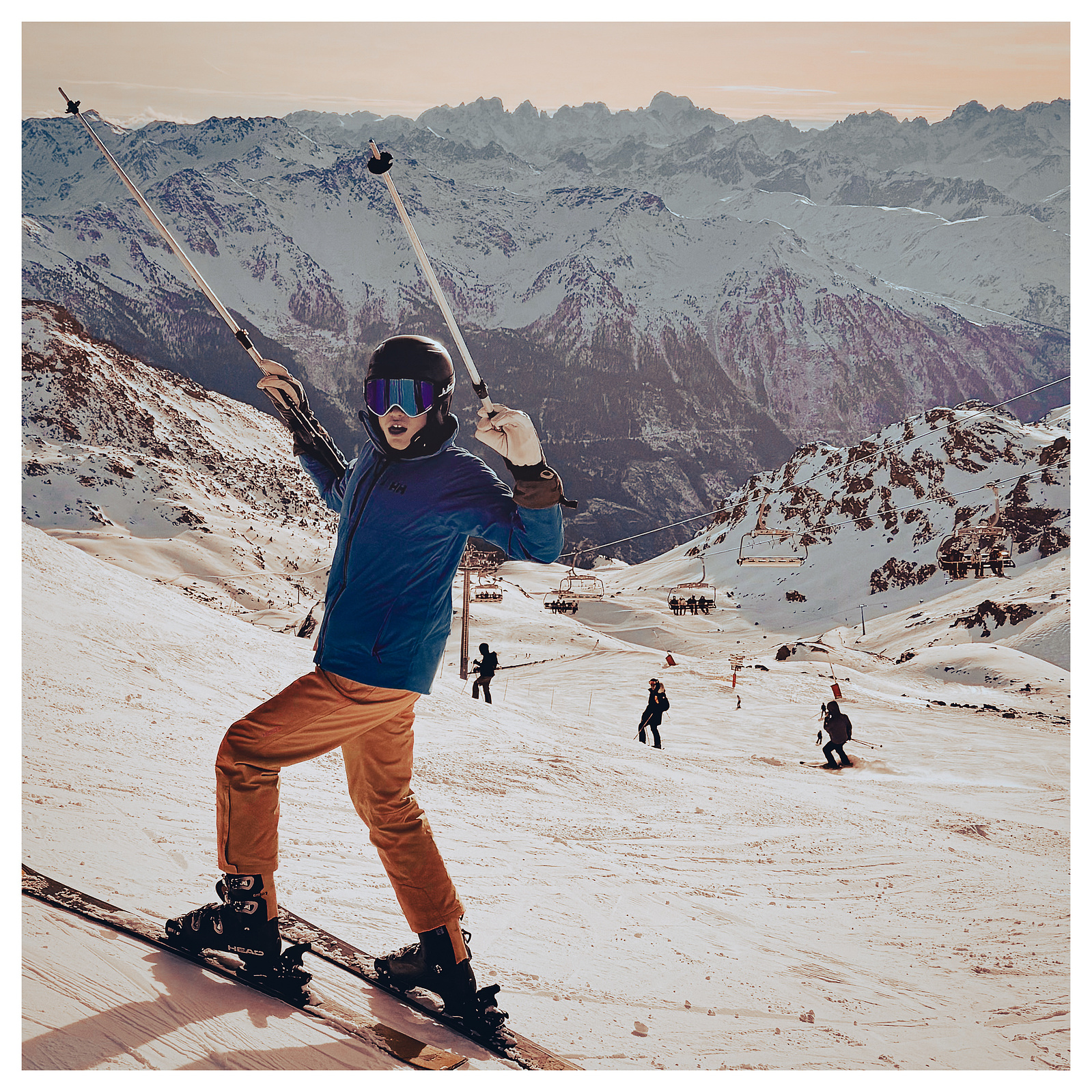 Boy in ski gear stands at the top of the slope with a dusky sky and mountains in the background