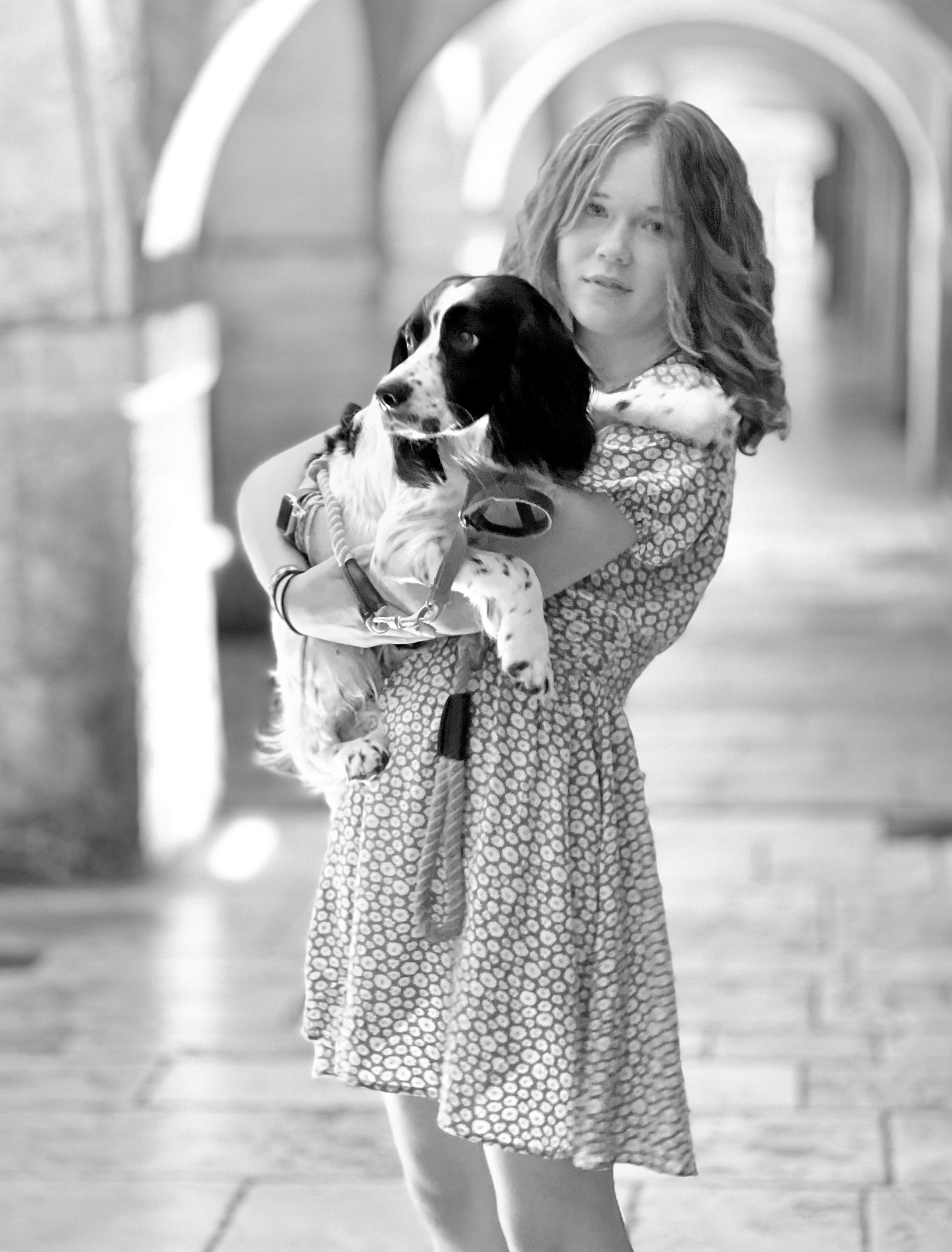 A girl stands holding her dog, a Springer Spaniel. She is in a covered area on the streets of La Rochelle France, with a series of arches