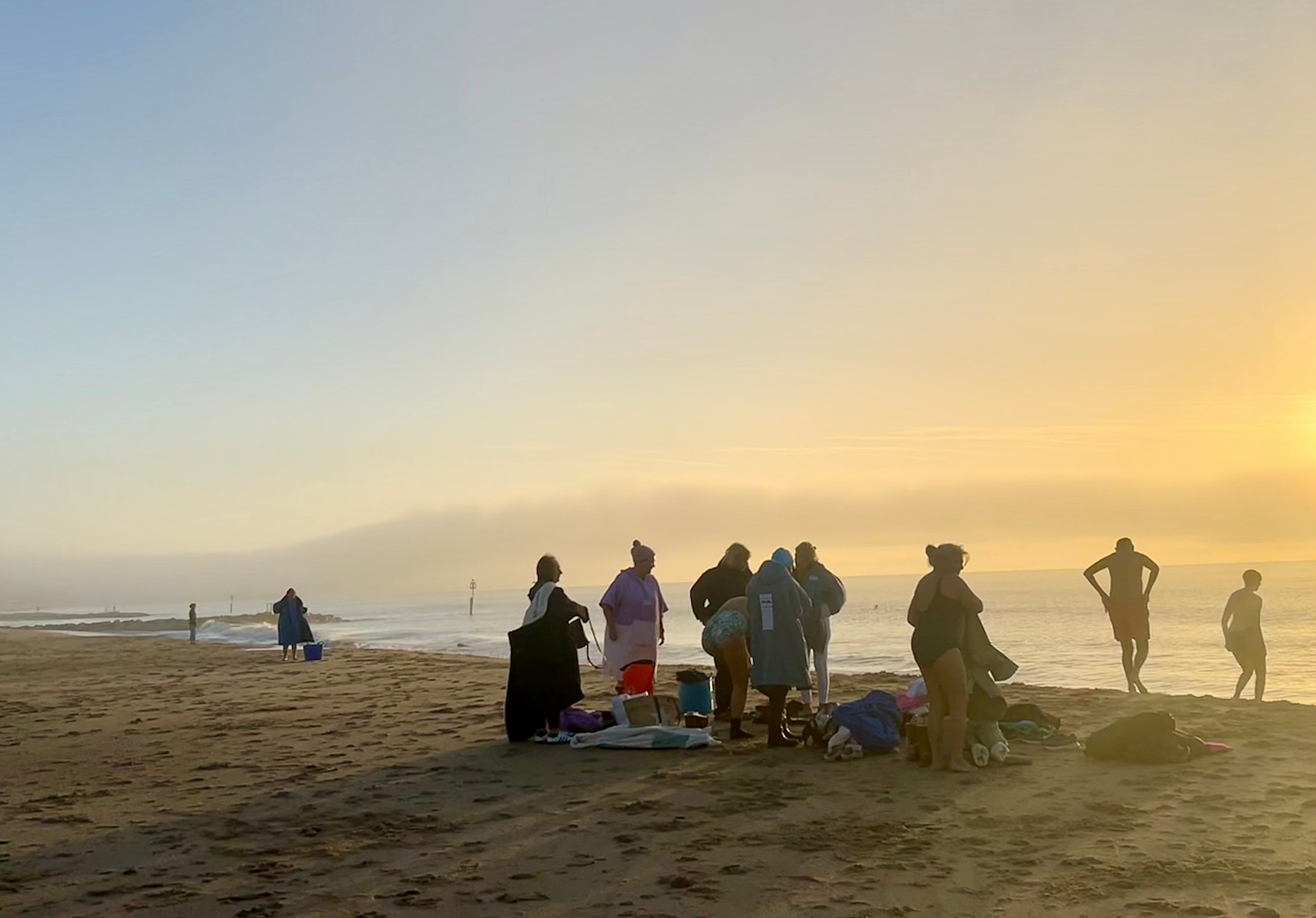 A group of swimmers wearing Dry Robes gather on the beach and prepare to enter the sea as the sun rises