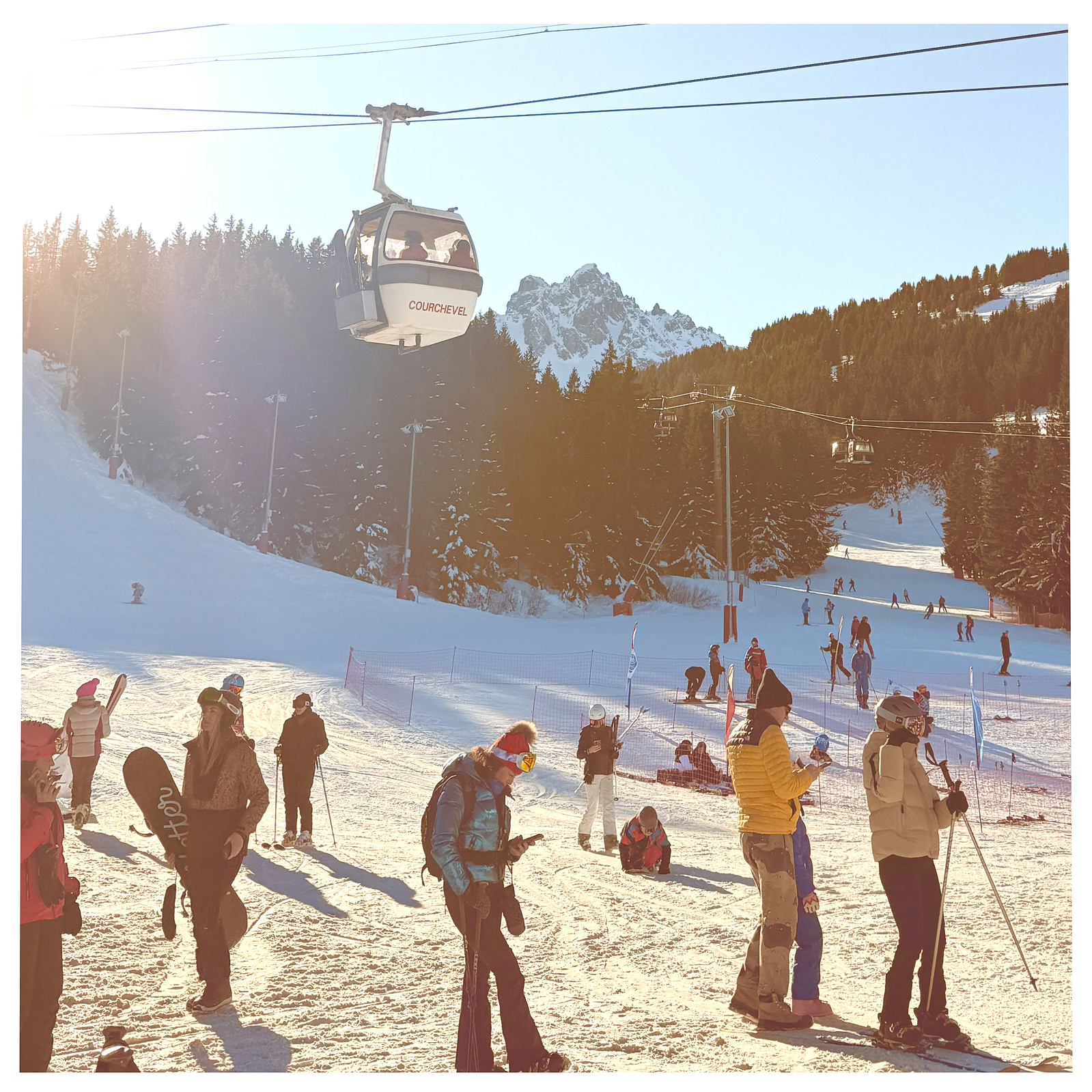 Group of skiers at the base of Courcheval all stand looking at their phones, oblivious to the beauty around them