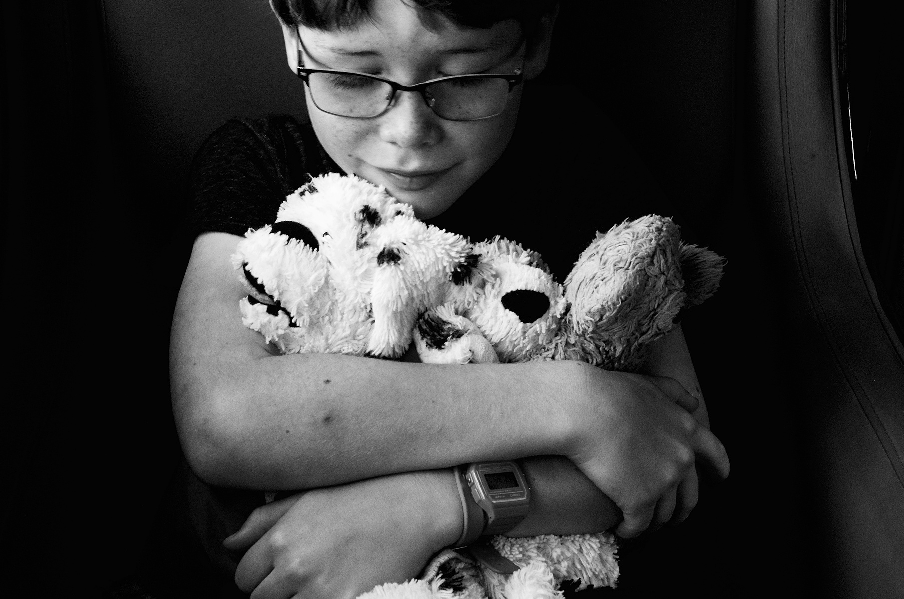 A young boy with glasses, sits on a train hugging and looking down on three of his favourite stuffies (Soller, Mallorca)