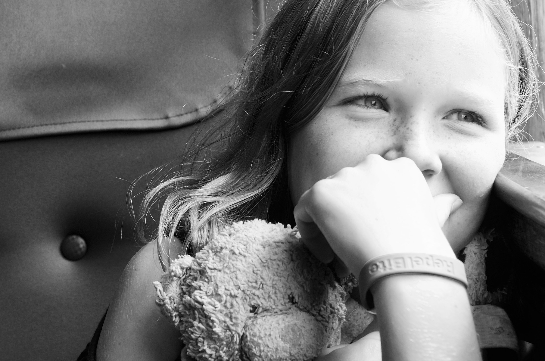 A young girl, sits on a train, looking out of the window, slightly smiling and hugging her favourite "teddy" (Soller train station, Mallorca)