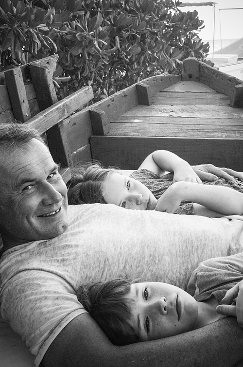 Dad with his two kids in a boat; he is smiling, the kids look enigmatic, bored, unimpressed and are looking off to the distance