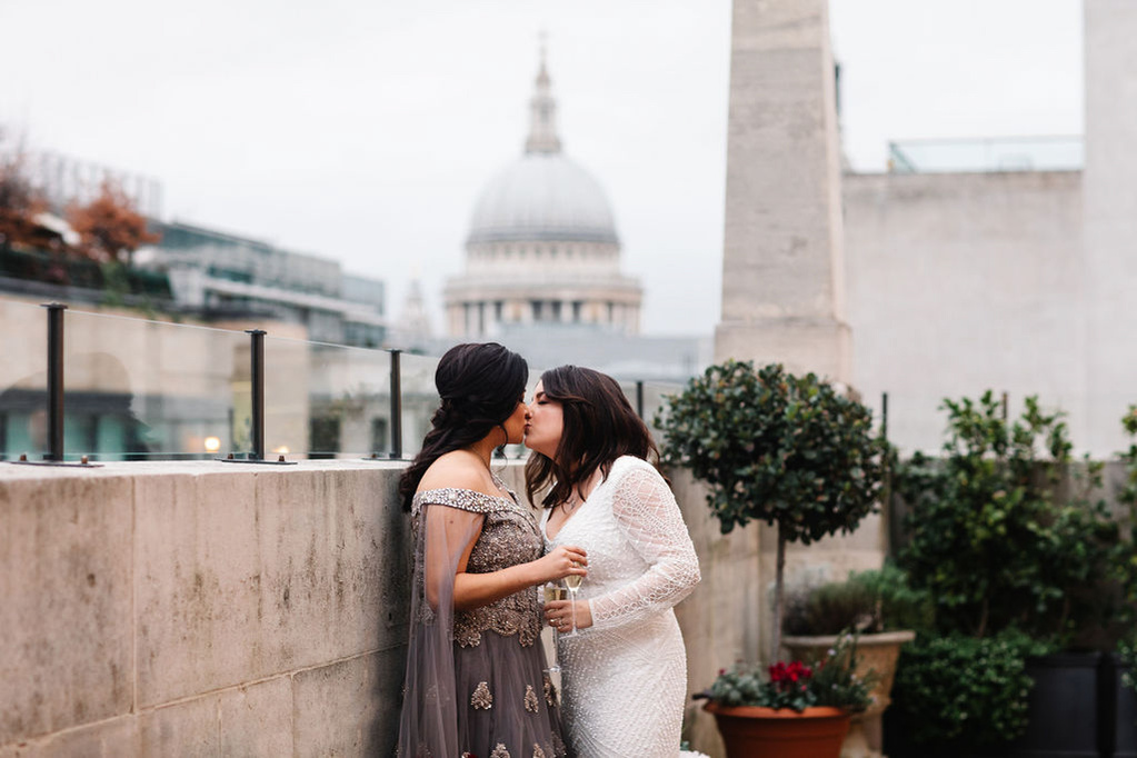 Two women kissing on the balcony of The Ned Hotel in London with St. Pauls Cathedral in the background 