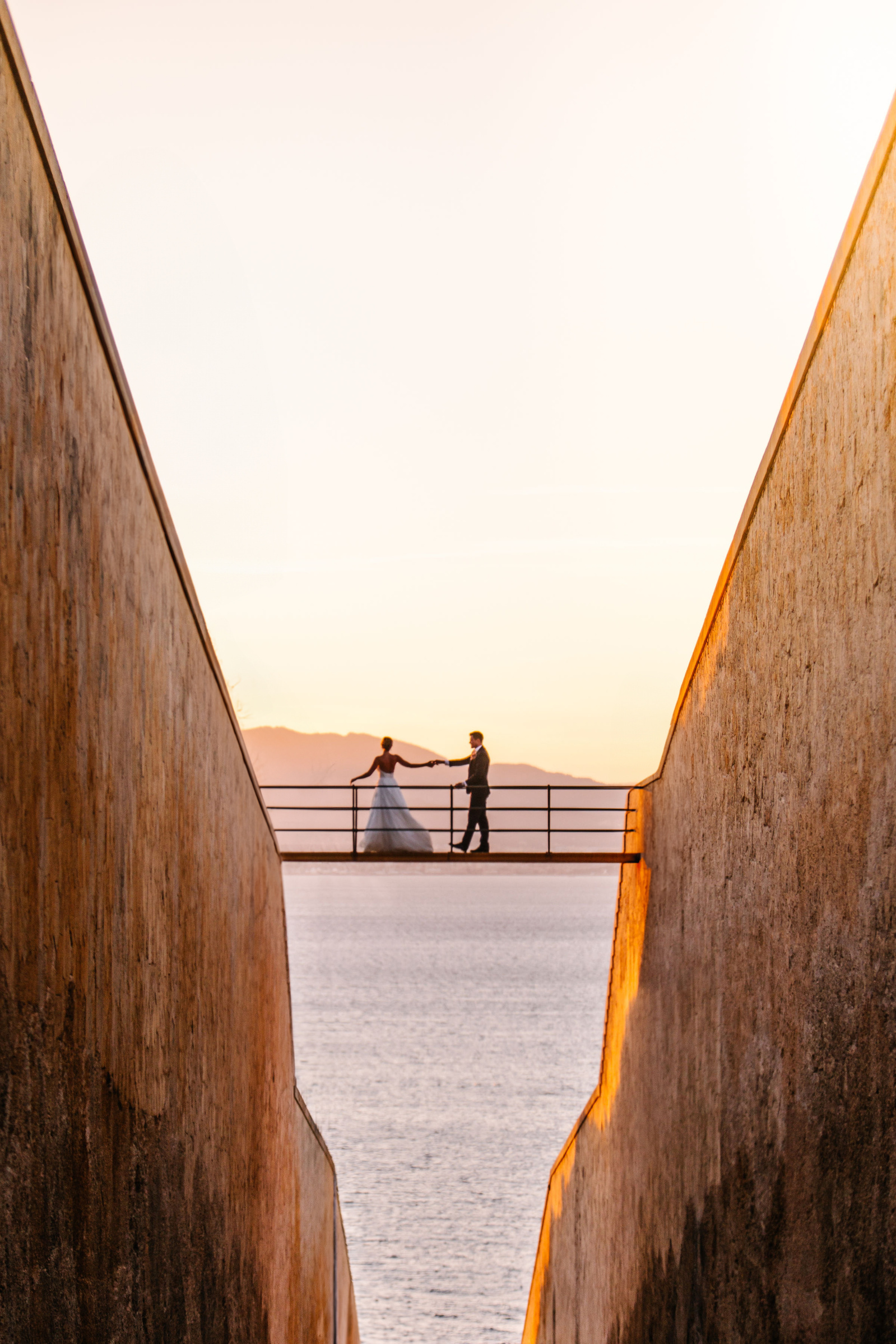 Couple on a bridge in Mallorca hand in hand against a sunset backdrop 