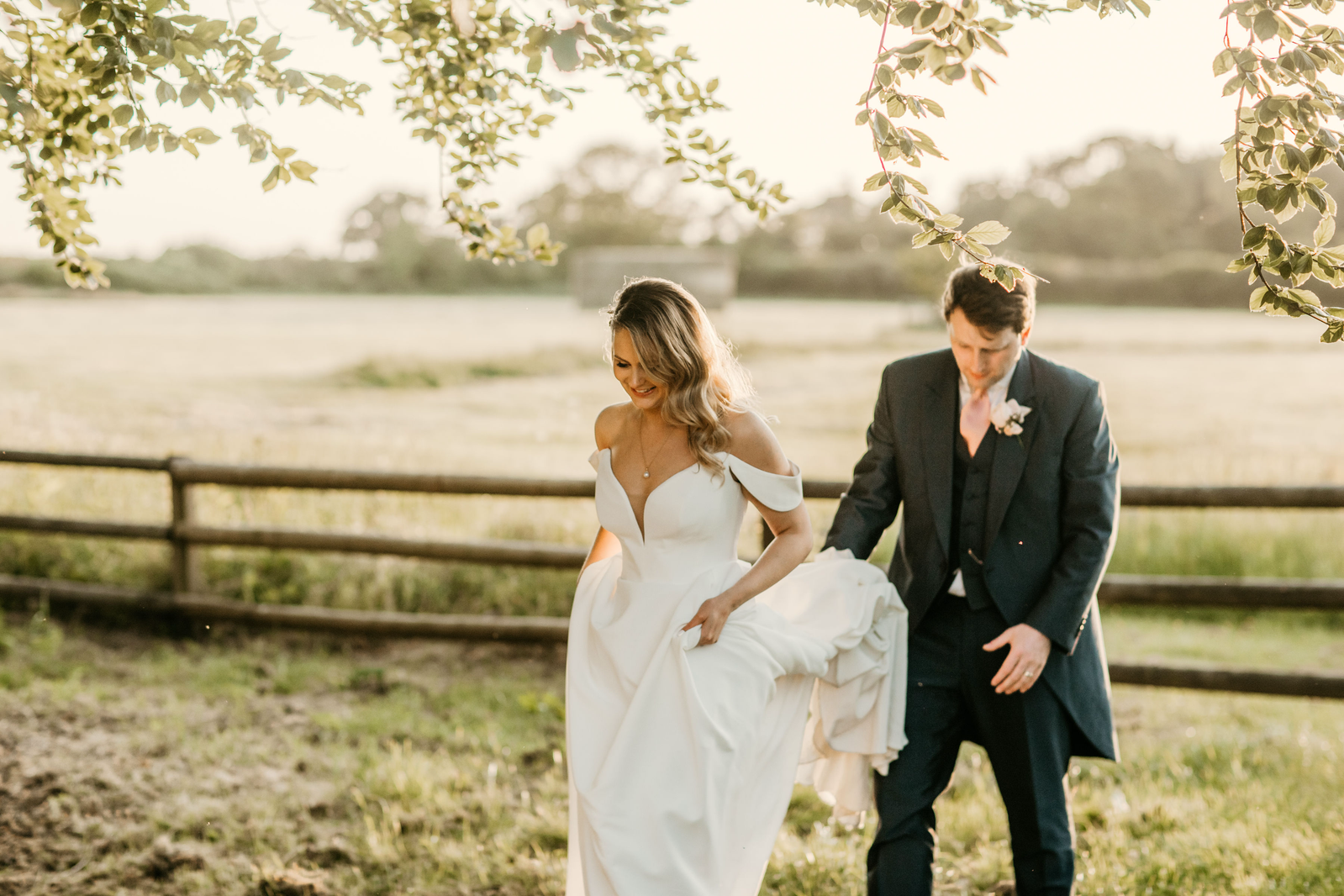 Couple crossing a bridge over a stream in a field in the Cotswolds on their wedding day 