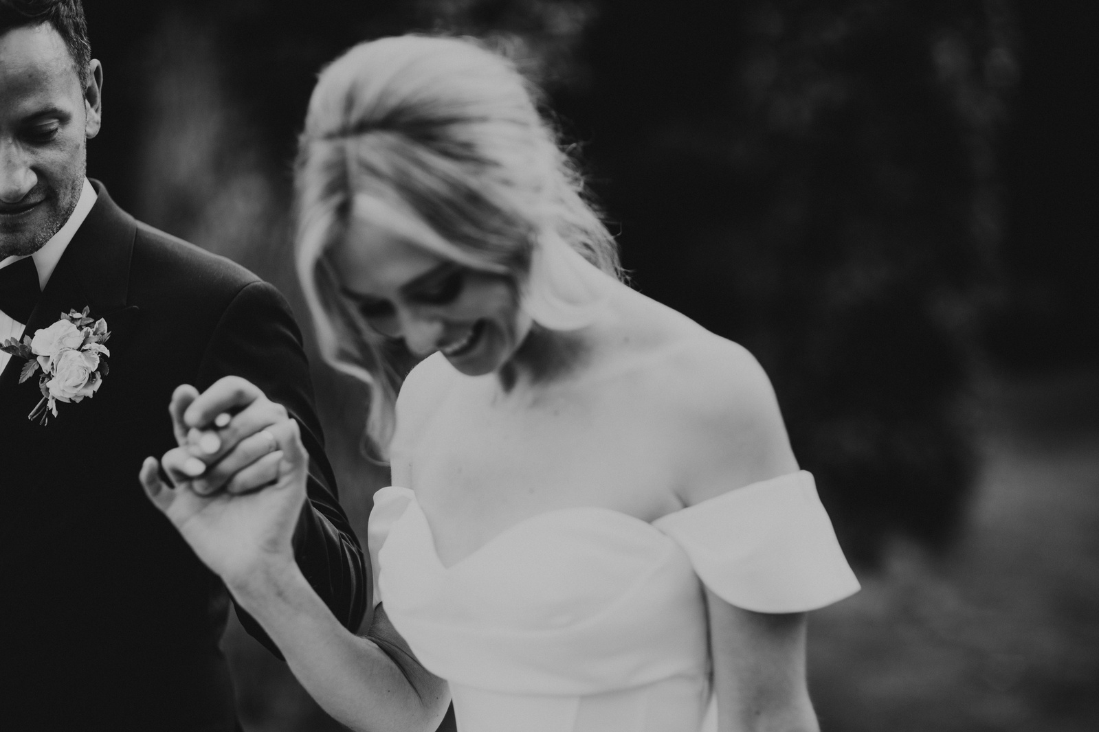 Black and white image of a couple holding hands, laughing with each other after just getting married