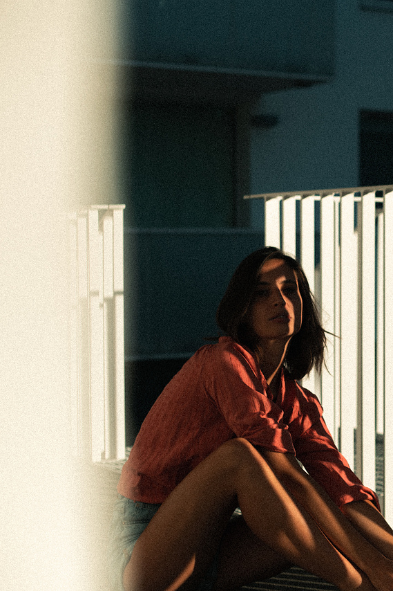 Photo cinématographique d'une fille assise à terre , à l'extérieur, devant sa chambre de motel, en fin de journée.