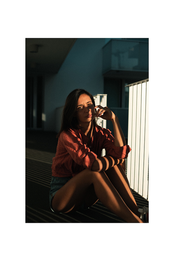 Photo cinématographique d'une fille assise à terre , à l'extérieur, devant sa chambre de motel, en fin de journée.