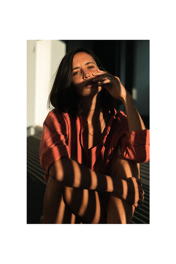 Photo cinématographique d'une fille assise à terre , à l'extérieur, devant sa chambre de motel, en fin de journée.