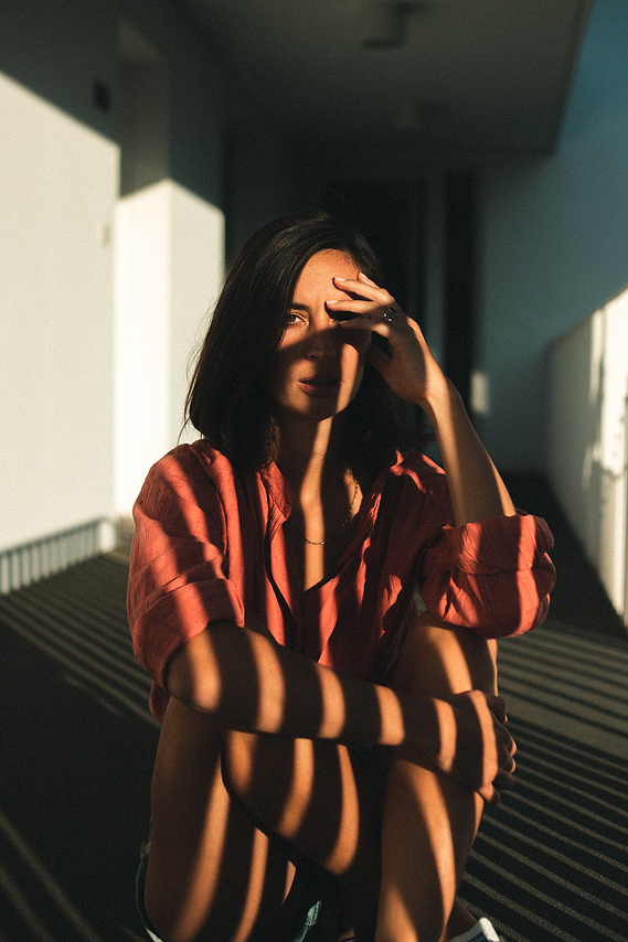 Photo cinématographique d'une fille assise à terre , à l'extérieur, devant sa chambre de motel, en fin de journée.