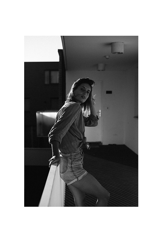 Photo cinématographique d'une fille appuyé sur la rambarde, à l'extérieur, devant sa chambre de motel, en fin de journée.
