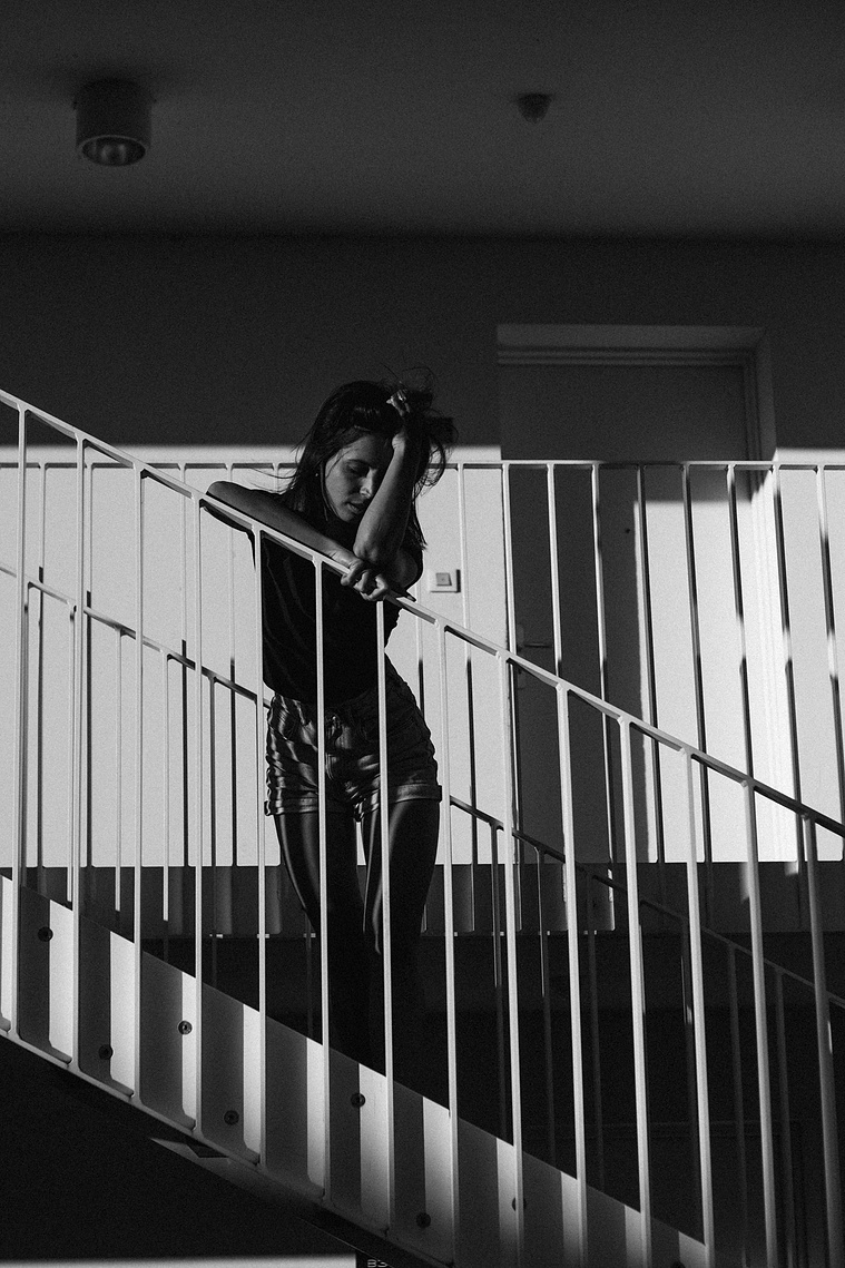 Photo cinématographique d'une fille appuyée sur la rambarde, devant sa chambre de motel, en fin de journée.
