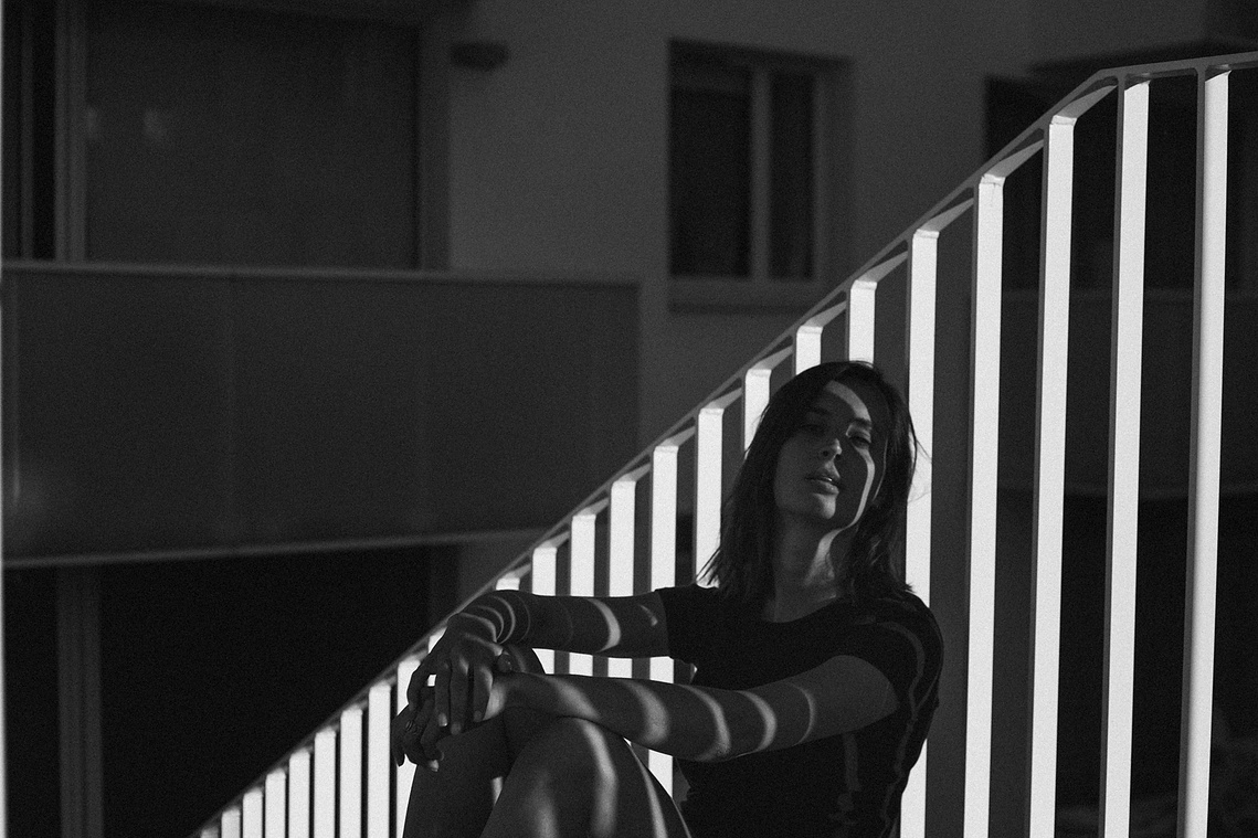 Photo cinématographique d'une fille assise à terre , à l'extérieur, devant sa chambre de motel, en fin de journée.