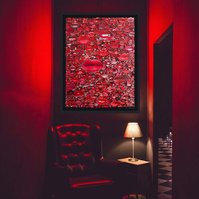 In-situ of large contemporary art collage entitled Gloss by Tasmanian visual artist Diane Allison of HALLISON Studios featuring hundreds of red pouting lips from magazines against a black ground, in a bar/night club with red lighting and black club chair.
