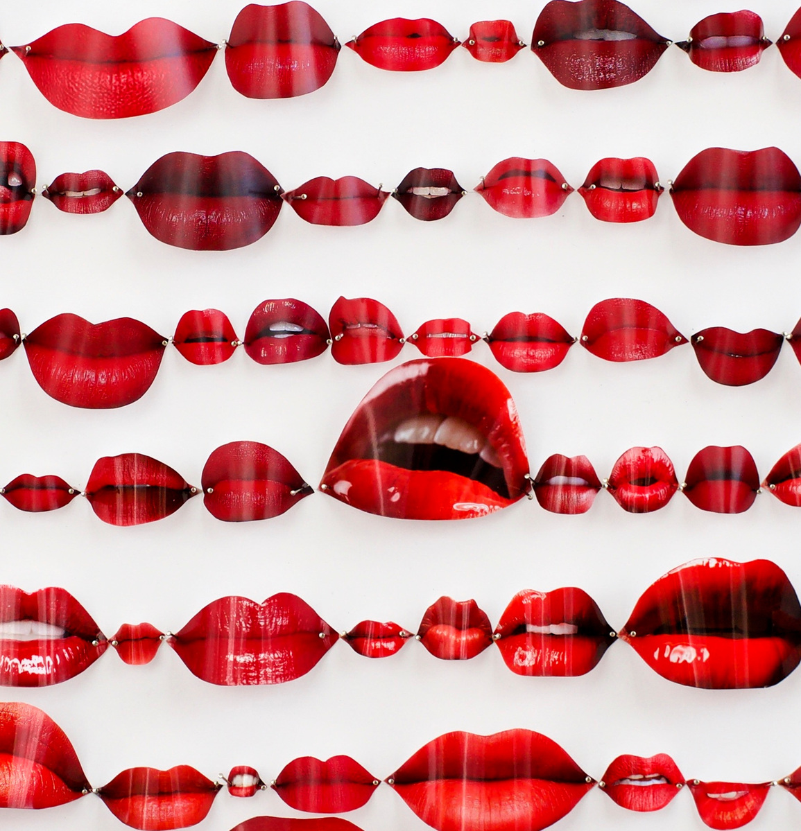 Close up image of Speechless, contemporary art work of red lips from fashion magazines Vogue, Elle, Harpers Bazaar and Net-a-Porter. They are pinned in rows like specimens on a white background. Visual artist Diane Allison, HALLISON Studios, Tasmania.