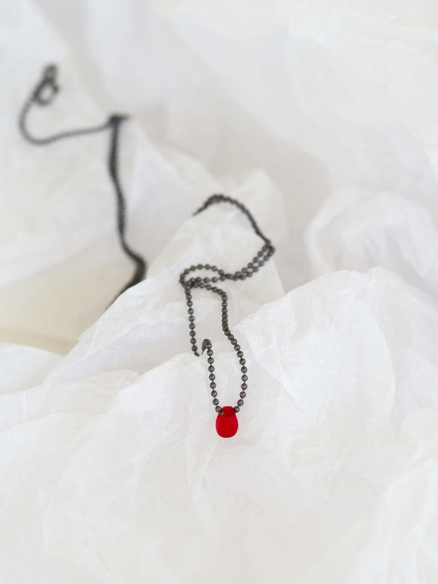 Sleeping Beauty pendant, contemporary jewellery by Diane Allison, HALLISON Studios, Tasmania. Oxidised sterling silver chain with a single blood red droplet, photographed on a white textured background like snow or ice.