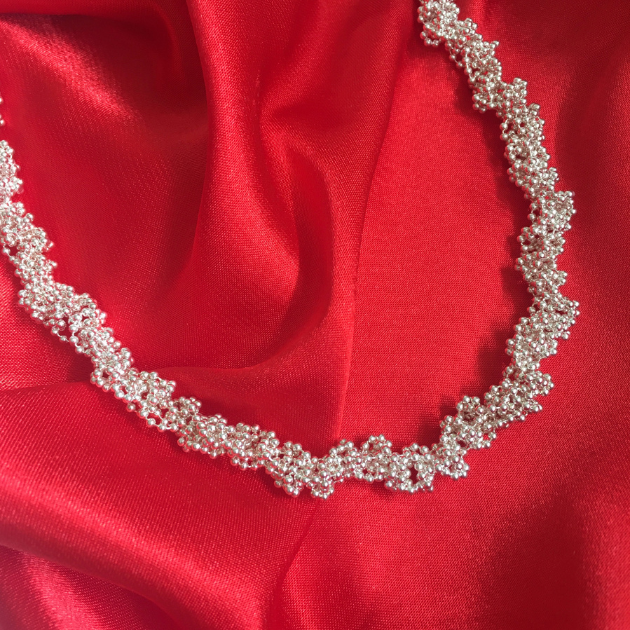 Classic style with a twist: the Twist necklace is a luxurious bright sterling silver necklace made by contemporary jeweller Diane Allison, HALLISON Studios, Tasmania, photographed against a rich red silk background.