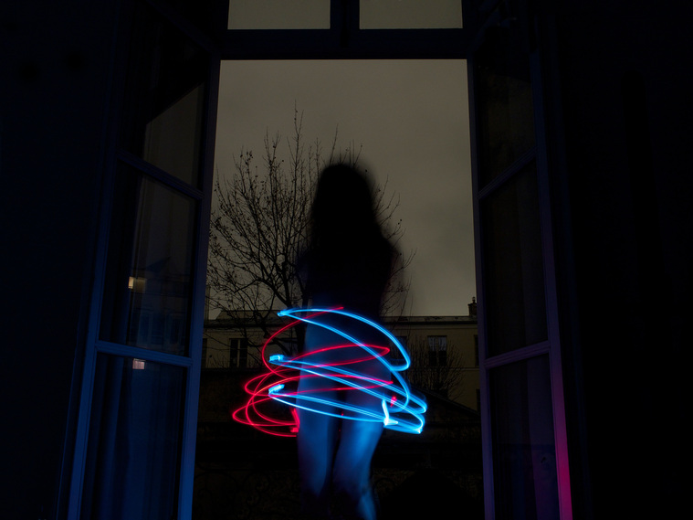Fine art photography by Di Allison, HALLISON Studios, Tasmania, online gallery store. Dark gothic portrait of a woman with long hair in front of French windows at night, red and blue light painting swirl around her called Scratched Upon Her Skin.