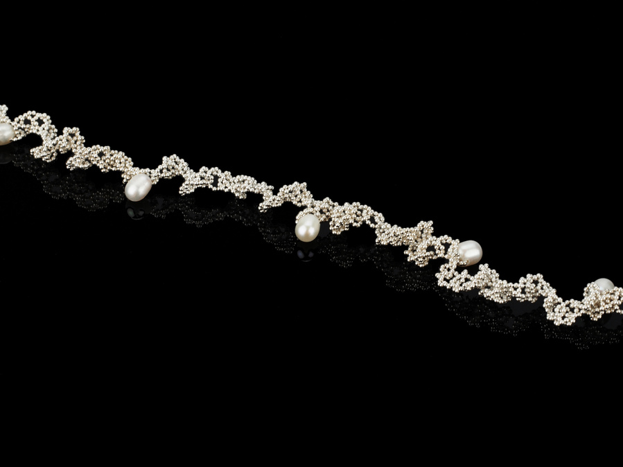 An intricate necklace of sterling silver and seven white freshwater pearl droplets on a black background by contemporary jeweller Diane Allison of HALLISON Studios, Tasmania, entitled Knitted Pearls. 
