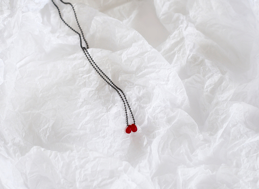Sleeping Beauty pendant, contemporary jewellery by Diane Allison, HALLISON Studios, Tasmania. Oxidised sterling silver chain with a single blood red droplet photographed on a white textured background like snow or ice.