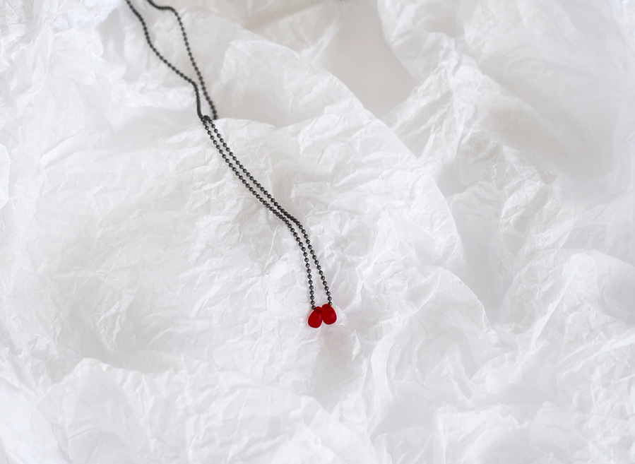 Sleeping Beauty pendant, contemporary jewellery by Diane Allison, HALLISON Studios, Tasmania. Oxidised sterling silver chain with a single blood red droplet photographed on a white textured background like snow or ice.