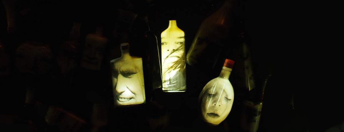 Detail of The Cloud by Tasmanian artist Patrick Hall featuring the illuminated faces of Patrick Hall, Diane Allison and son Austin on suspended spirit bottles hovering in darkness