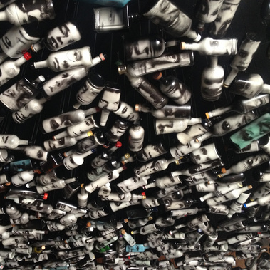 The Cloud art installation by Tasmanian contemporary visual artist Patrick Hall at Dark MOFO 2016 using 1016 spirit bottles with illuminated faces on each, suspended from the ceiling, dripping with tears, hovering in darkness with soundscape, Hobart.
